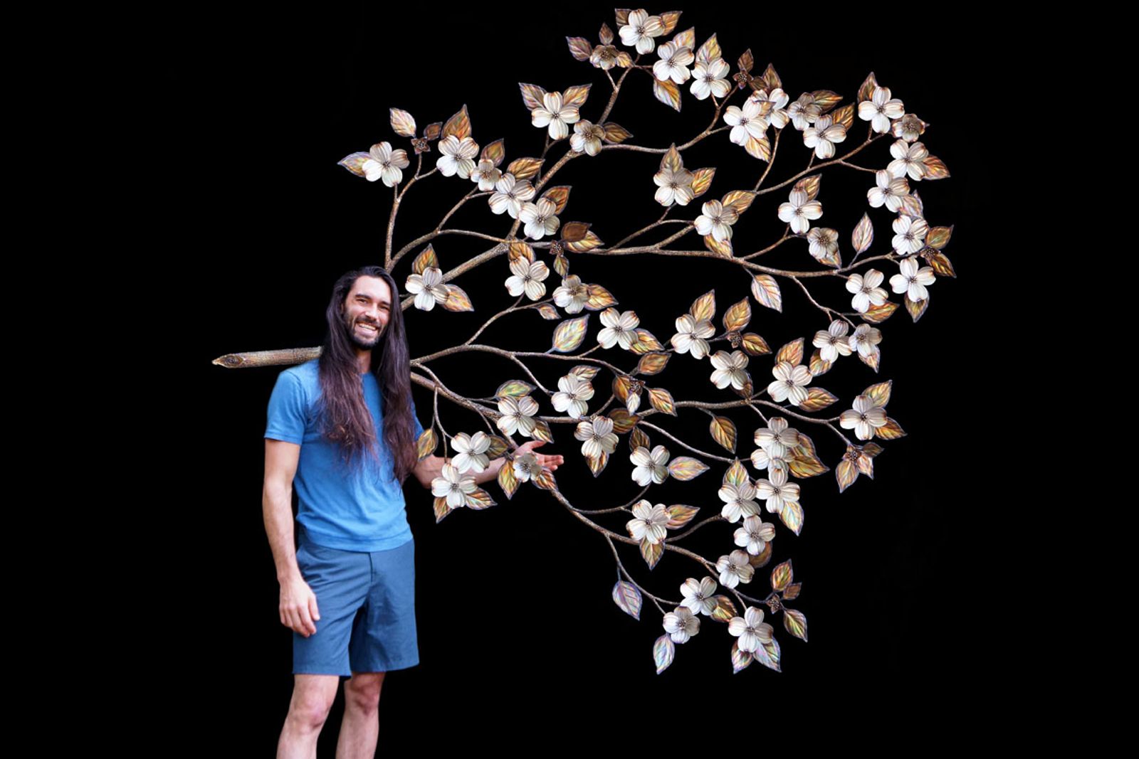 Artist Aiden Dale with his large stainless steel dogwood sculpture for scale.