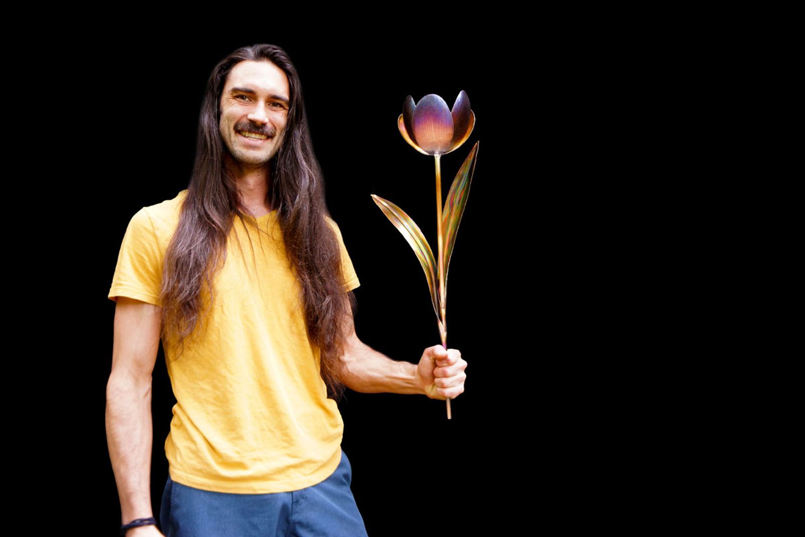 Artist Aiden Dale holding his stainless steel tulip sculpture, handmade with torch patina and intricate grinder detailing.