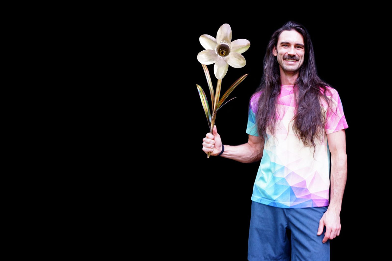 Artist Aiden Dale holding his stainless steel daffodil sculpture with polished silver petals and torch-colored stem and leaves.