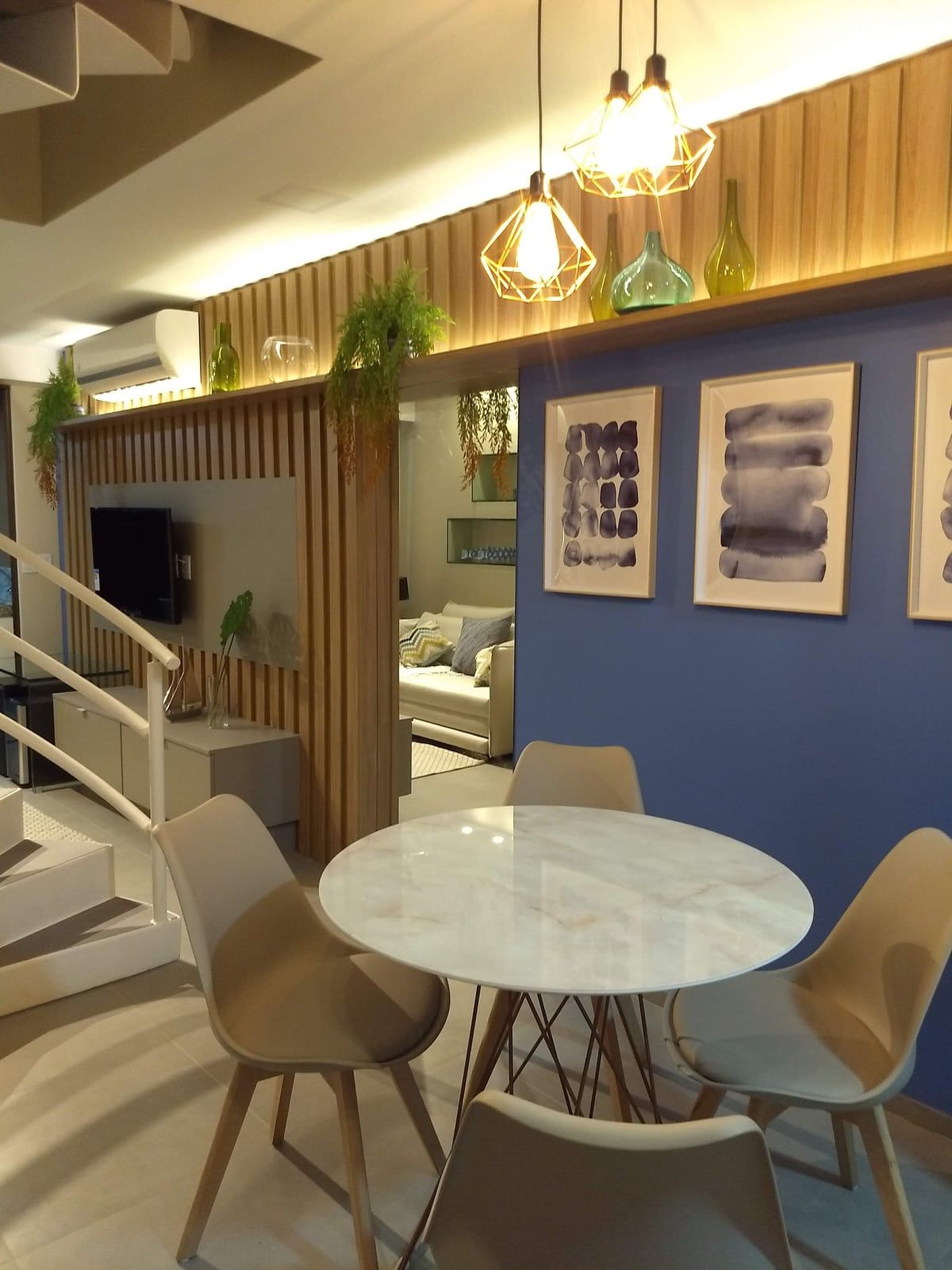 Jantar integrado ao living, com escada caracol e quadros sobre a parede azul