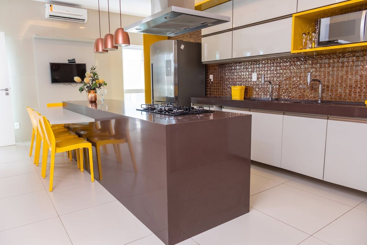 Cozinha com ilha, cooktop e pastilhas em cobre, com banquetas amarelas