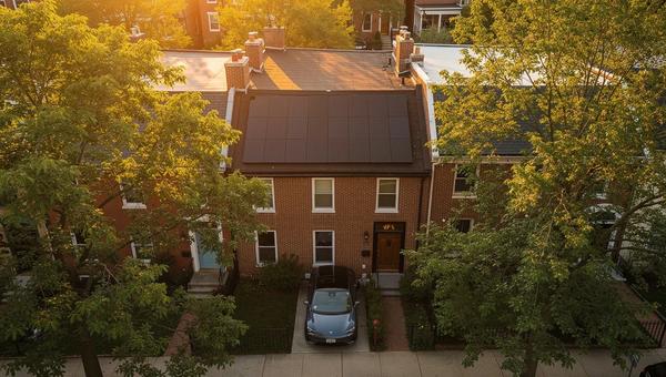 Solar panels on a DC row house roof with an electric vehicle parked in the driveway below