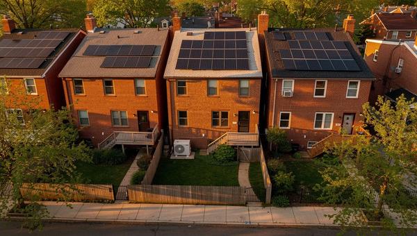Solar panels on a DC row house roof with a heat pump outdoor unit visible in the alley below
