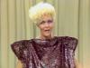 Jeanne Little is talking. She is wearing huge shoulder pads in her dress and blue eye make-up.