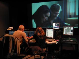 Two editors seated behind a bank of controls and watching a timecoded sequence from an Australian film on a large screen.