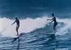 Still frame of two surfers riding a wave.