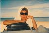 Bronwyn Murphy seated on a beach, with her arm resting on a black bag and a towel wrapped around her head.