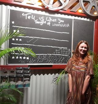 Jazz Money standing next to a chalkboard with audience scores for the film WINHANGANHA