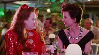 A scene from Muriel's Wedding with Toni Collette and Rachel Griffiths seated and looking directly at each other. They are both dressed up for a night out.