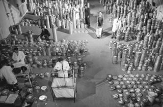 A black and white image of a room filled with hundreds of film canisters and mean in lab coats inspecting them.