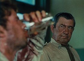 A policeman watches a grubby man covered in sweat and grime downing a glass of beer