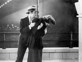 A man clutching a woman on a footpath under a bridge in a scene from the 1938 movie Broken Melody.