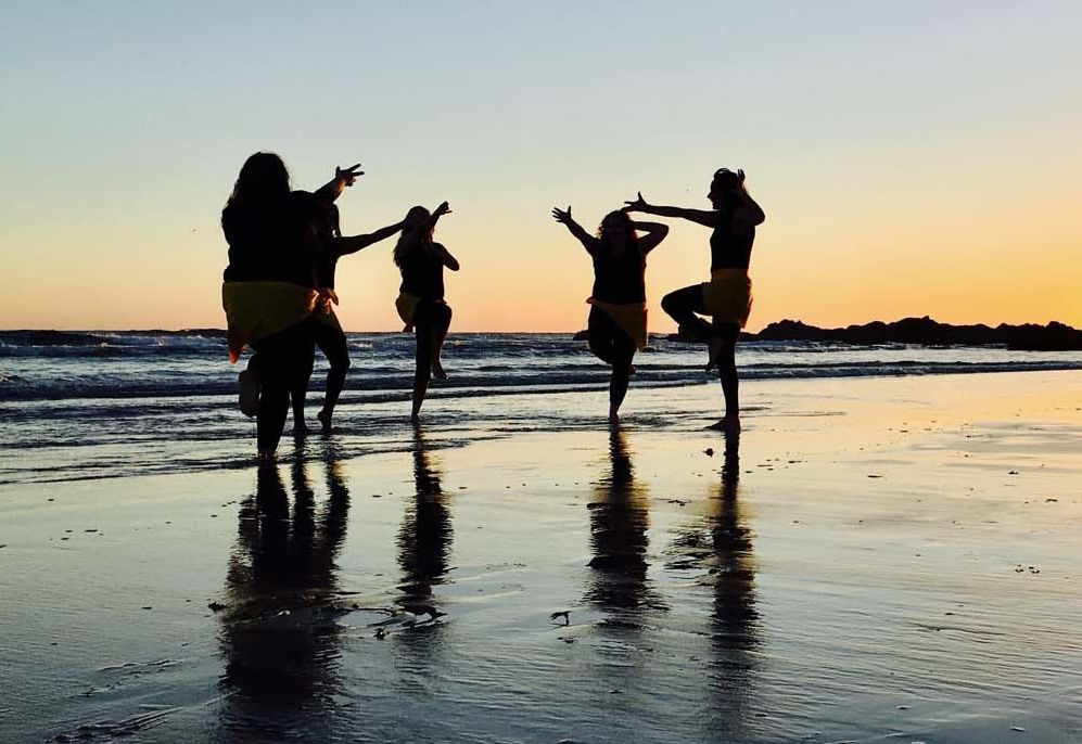 Five First Nations dancers on a beach.