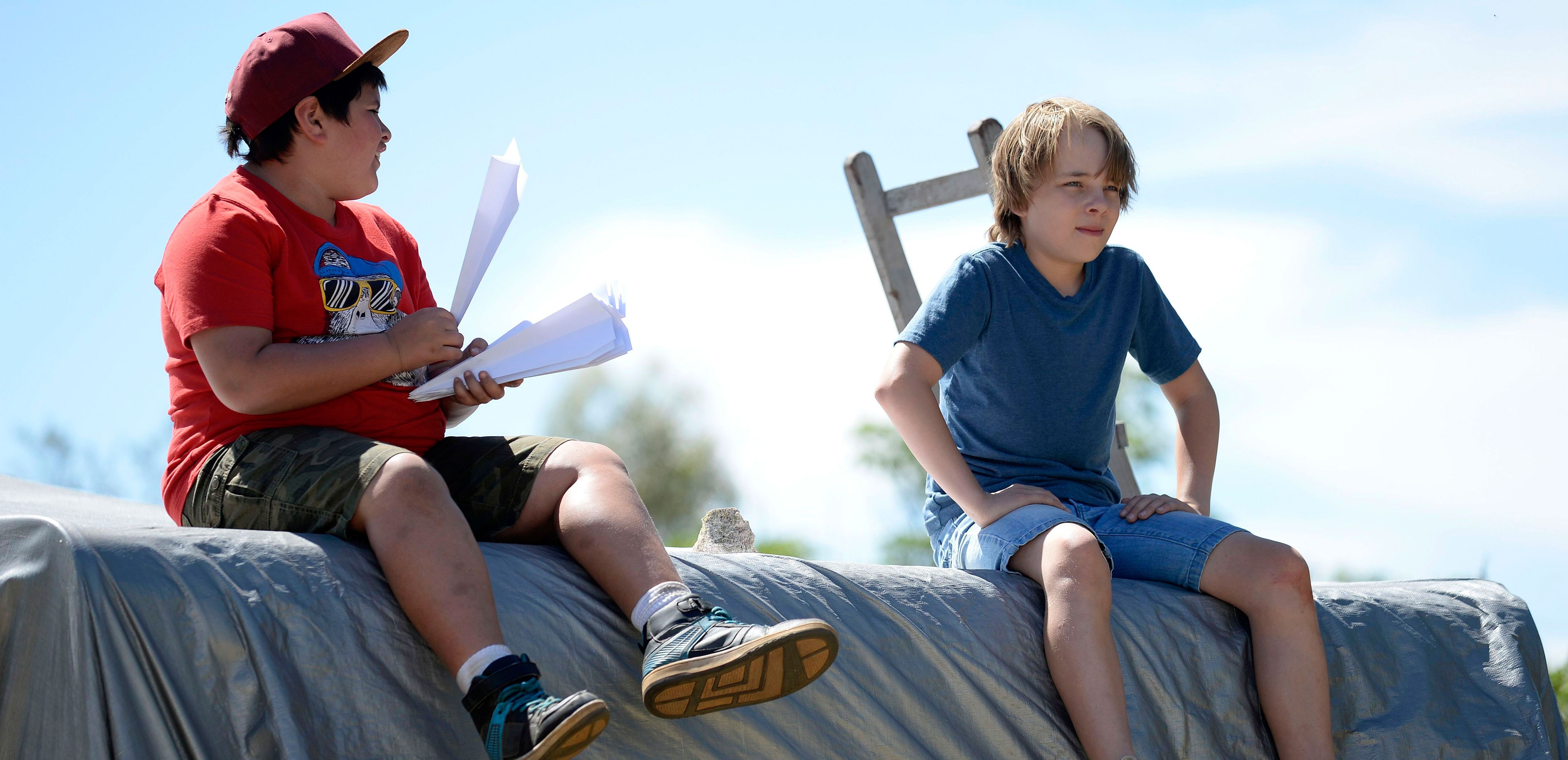 Two boys sit next to each other, with one holding a bunch of paper planes.