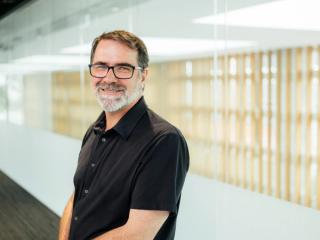 Professor Michael Dezuanni smiling. He is wearing a black short-sleeved shirt and smiling at the camera 