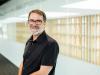 Professor Michael Dezuanni smiling. He is wearing a black short-sleeved shirt and smiling at the camera 
