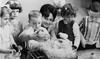 A group of small children standing around a seated young woman looking at baby chickens.