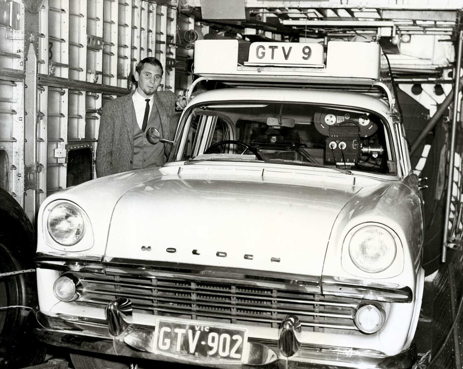 A man standing next to a Holden car with a TV camera mounted on top and a sign for GTV9