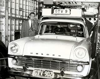 A man standing next to a Holden car with a TV camera mounted on top and a sign for GTV9