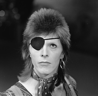 David Bowie wears an eye patch on one eye. He is looking up.