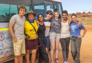 The cast and director of 'Sweet As' standing arm in arm in the outback, in front of a mini van.