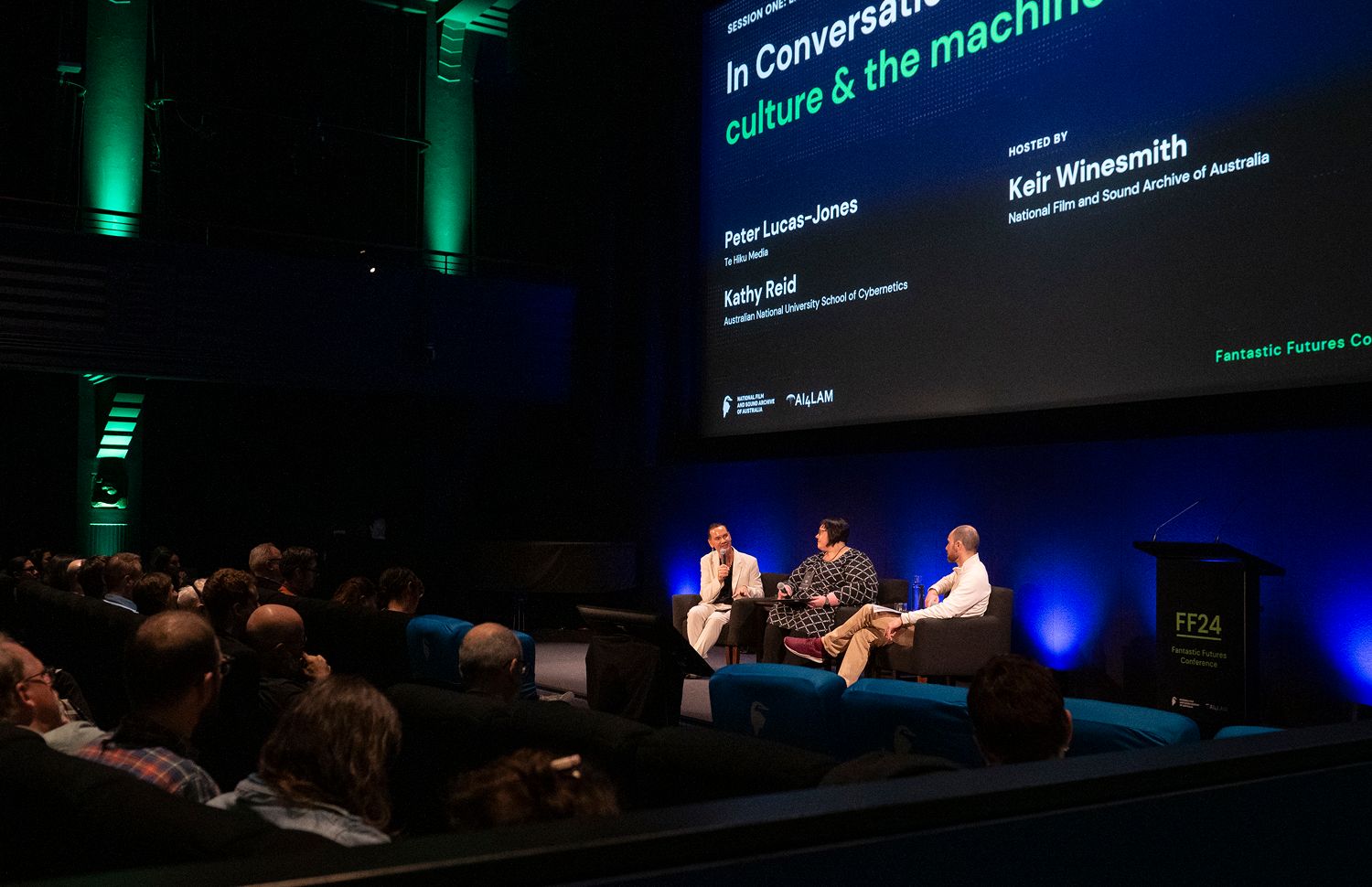 Peter-Lucas Jones, Kathy Reid and Keir Winesmith presenting a panel on a stage