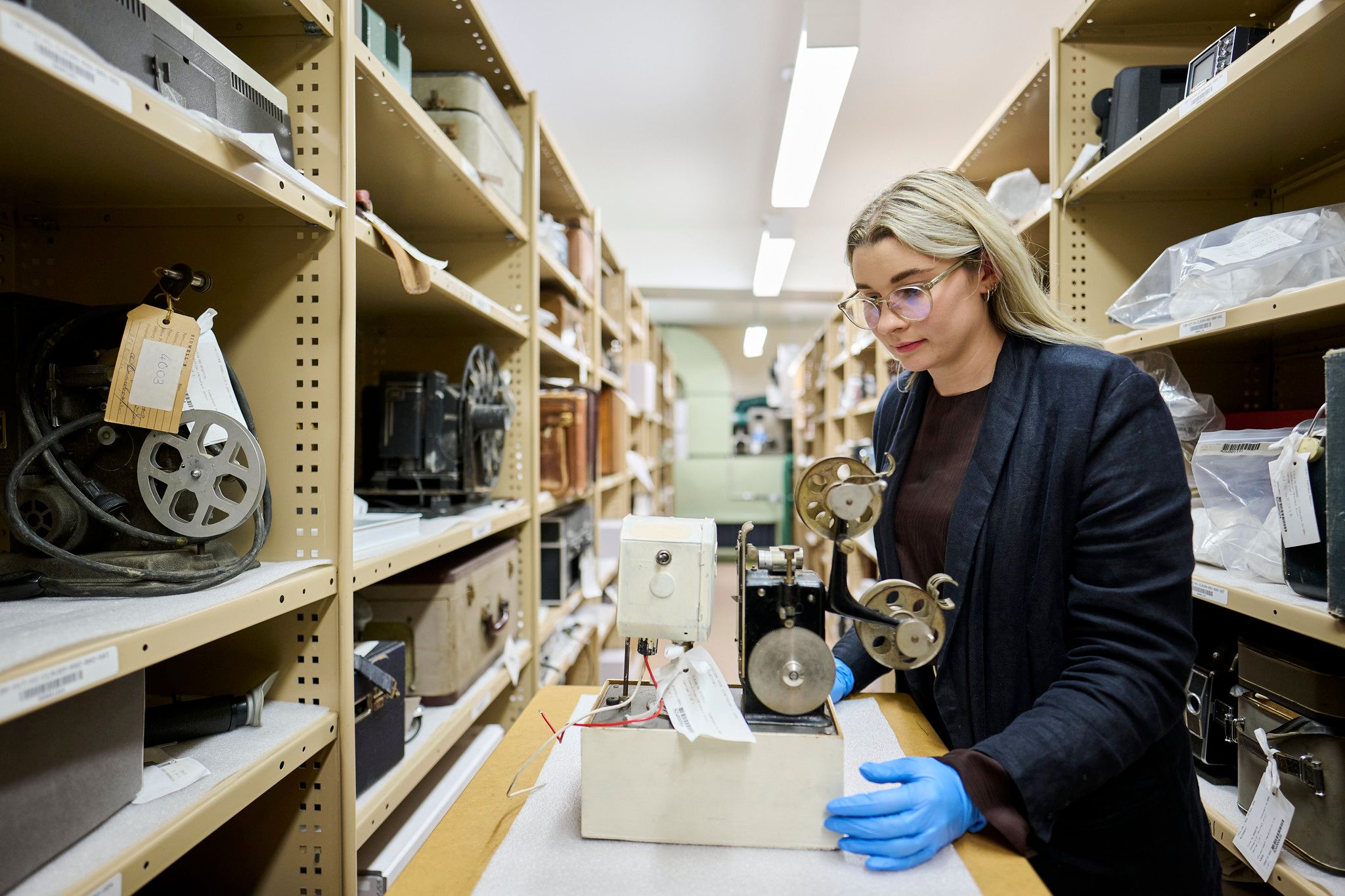 A woman wearing gloves examines an old film projector.