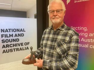 Retired TV journalist holding his Logie Award in the offices of the National Film and Sound Archive.