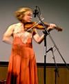 A woman in a red dress playing a violin on stage.