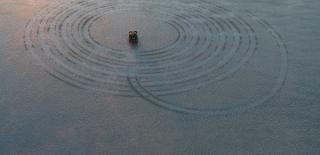 A four-wheel drive making a large spiraling tyre track in the sand.