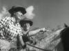 Film still of a woman and a man on horseback. The man points into the distance