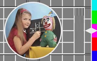 A young girl standing next to a chalkboard with a stuffed clown toy next to her, inset in a colour tv test pattern.