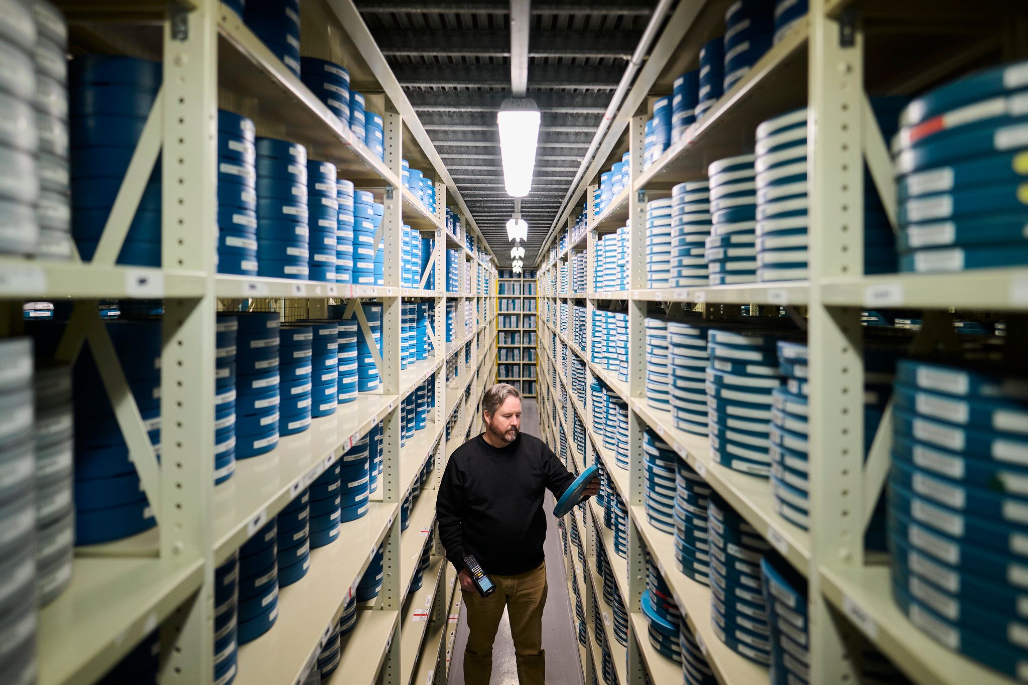 A man stands within two long shelving units filled with blue labelled film canisters.