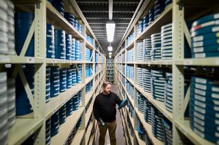 A man stands within two long shelving units filled with blue labelled film canisters.