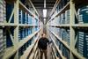 A man stands within two long shelving units filled with blue labelled film canisters.