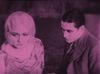 Pink tinted frame capture from the film, The Cheaters, shows aman and woman sitting by a lake