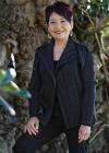 Annette Shun Wah standing outside in front of a tree, smiling and in a relaxed pose with one hand resting on her leg