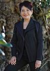 Annette Shun Wah standing outside in front of a tree, smiling and in a relaxed pose with one hand resting on her leg.