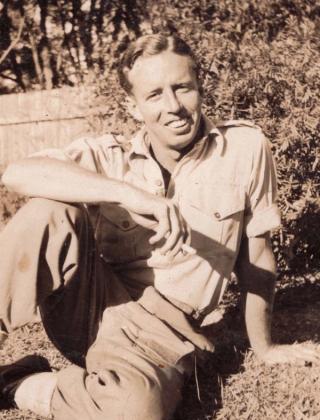 Composer James Joseph White seated on the grass and smoking a cigarette
