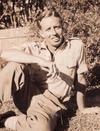 Composer James Joseph White seated on the grass and smoking a cigarette