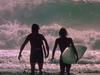 Two surfers holding their surfboards and standing before large waves.