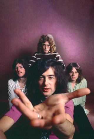 A posed studio portrait from 1969 of the four members of rock band Led Zeppelin. One of the band members stretches his hand out to the camera