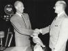 Two middle-aged men in suits shaking hands.