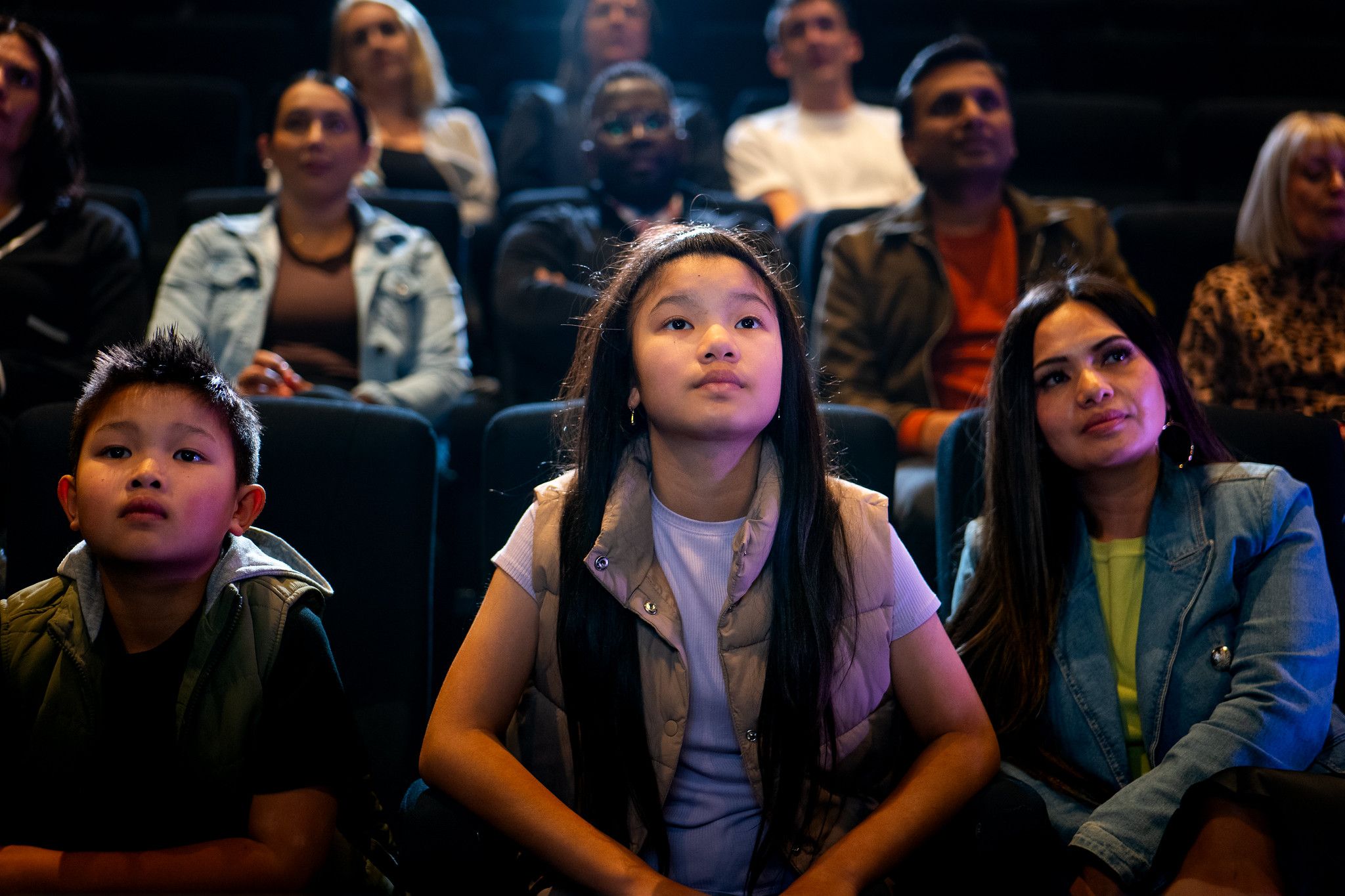 A boy, girl and woman sit in the middle of a busy cinema, staring up at a screen off camera.