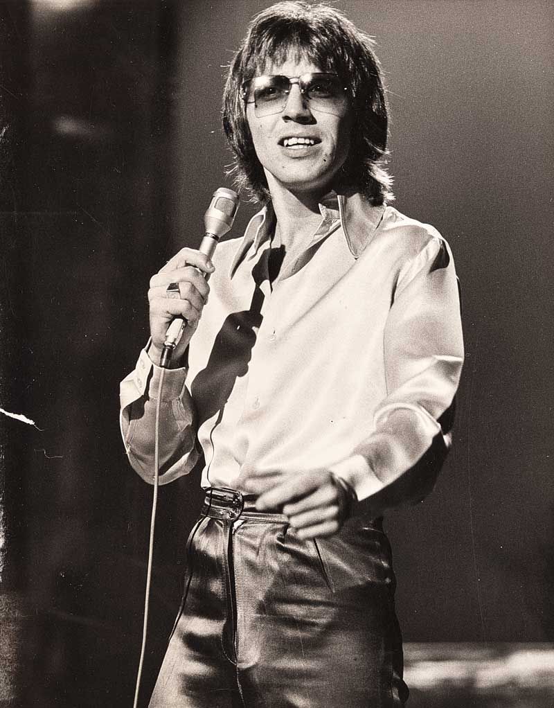 Three-quarter image of singer Stevie Wright holding a microphone and standing on a stage.