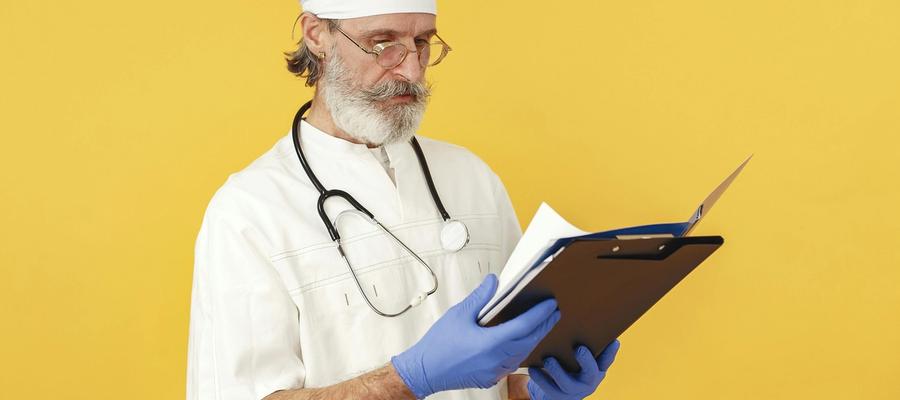 A Medicare doctor reviews patient medical records on a clipboard, wearing white scrubs, a surgical cap, and blue gloves.