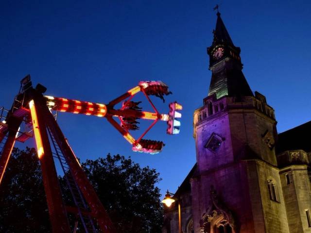 A crowded night scene at the Banbury Michaelmas Fair featuring illuminated amusement rides and fairground stalls under a dark sky.
