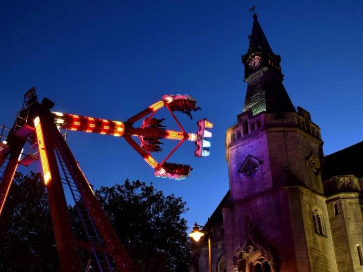 A crowded night scene at the Banbury Michaelmas Fair featuring illuminated amusement rides and fairground stalls under a dark sky.