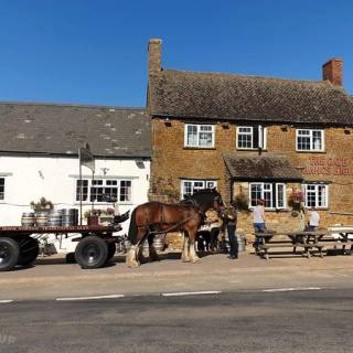 An exterior view of a historic stone pub in Chipping Norton featuring a traditional hanging sign and dark green painted storefront under a clear sky.