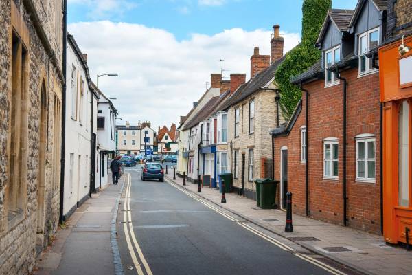 A quiet and charming street in Bicester town centre featuring traditional stone buildings and local storefronts under a soft blue sky.